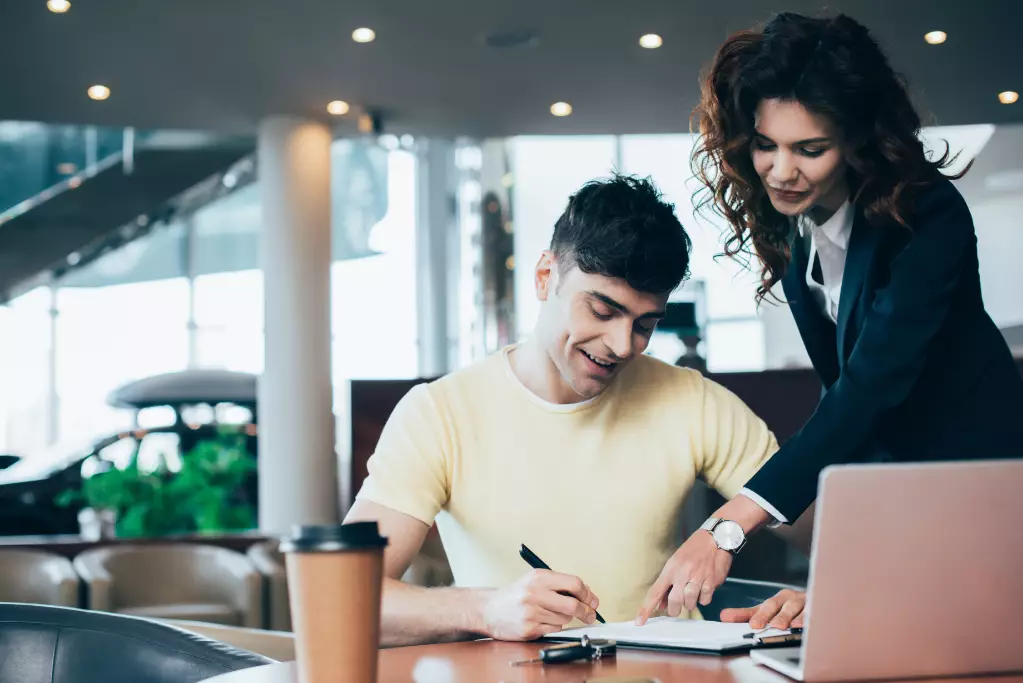 Selective focus of attractive car dealer and happy customer signing paper