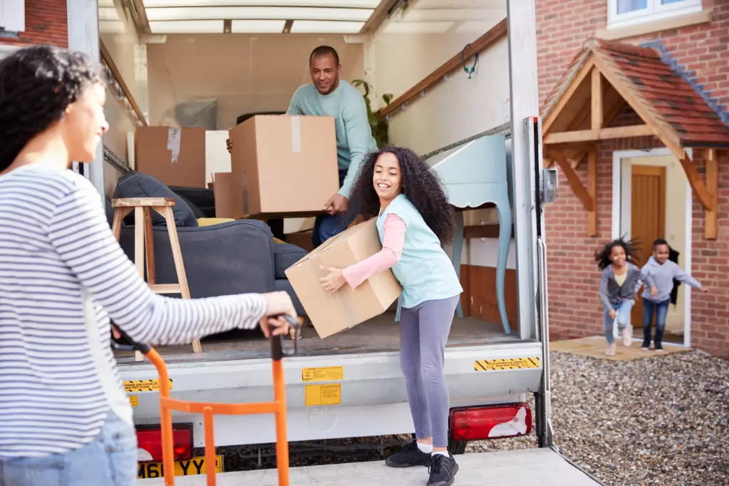 Family Unloading Furniture From Removal Truck Into New Home