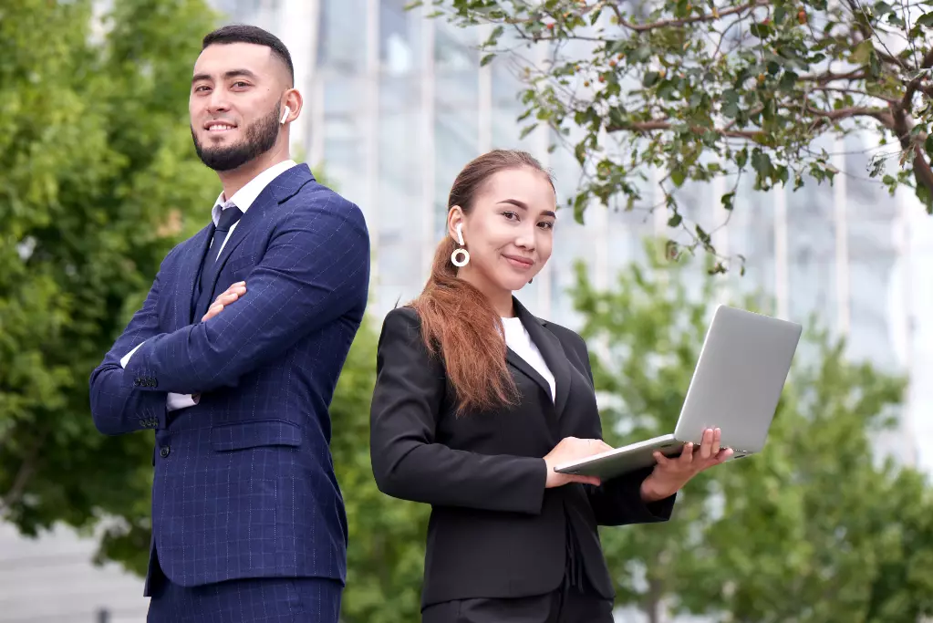 Businessman and businesswoman realtors with laptop outside, asian kazakh entrepreneurs discuss project